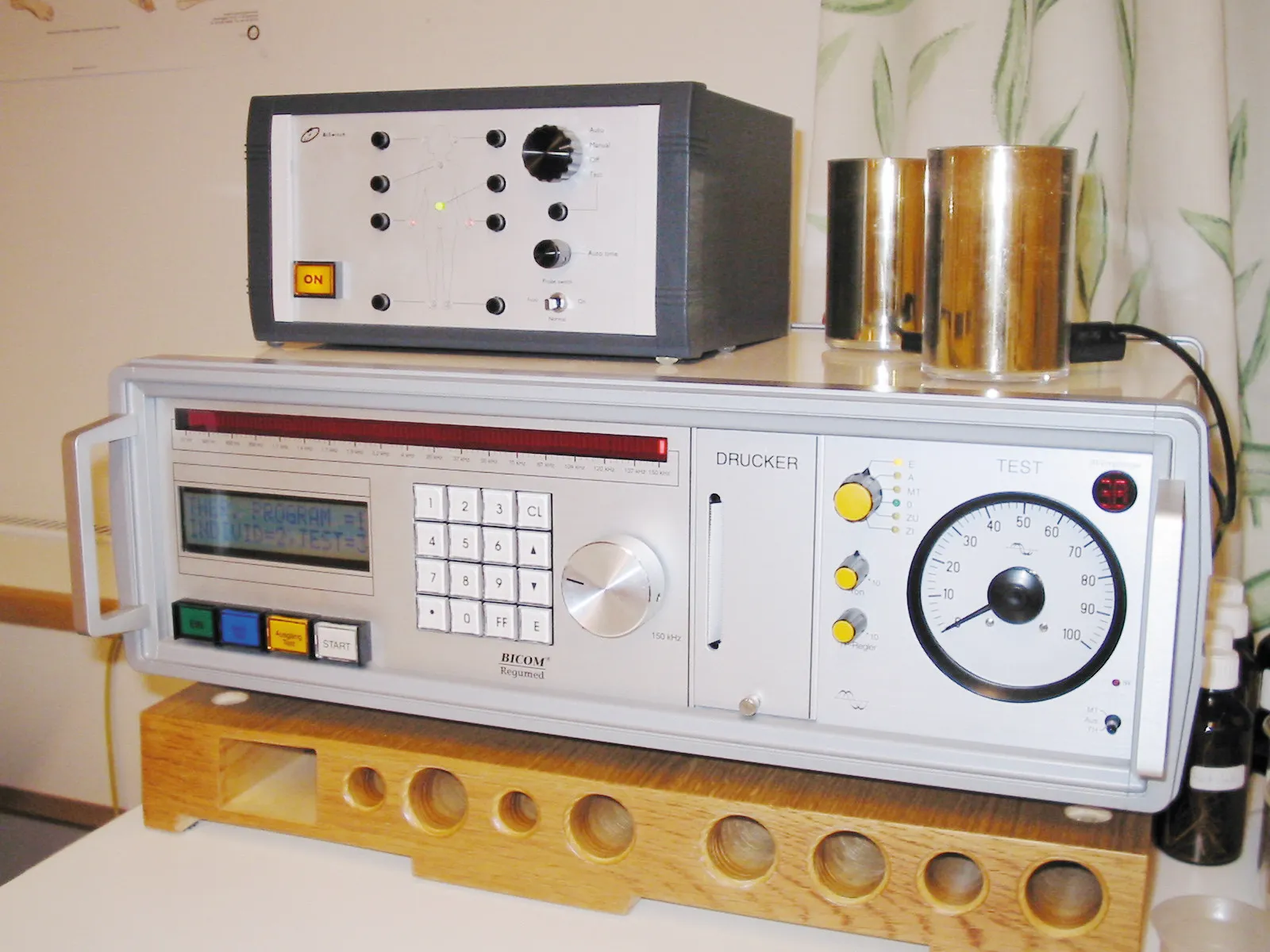 The electrode switch sitting on a BICOM Regumed instrument, its front panel a body diagram ringed with electrode sockets, beside an Auto/Manual/Off/Test selector