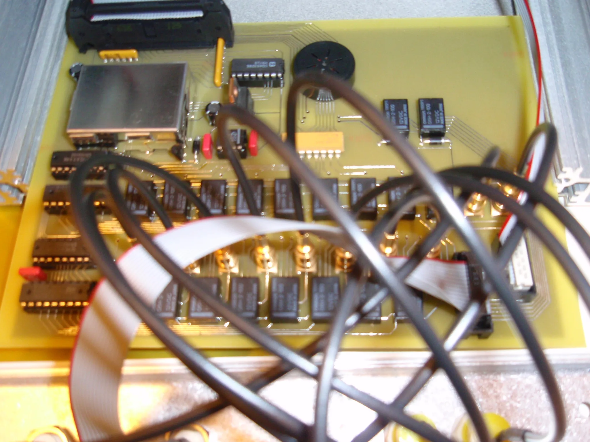 The main board from above: logic in sockets, a shielded module, a piezo buzzer, and a bank of Omron 12 V relays feeding the gold-plated jack sockets